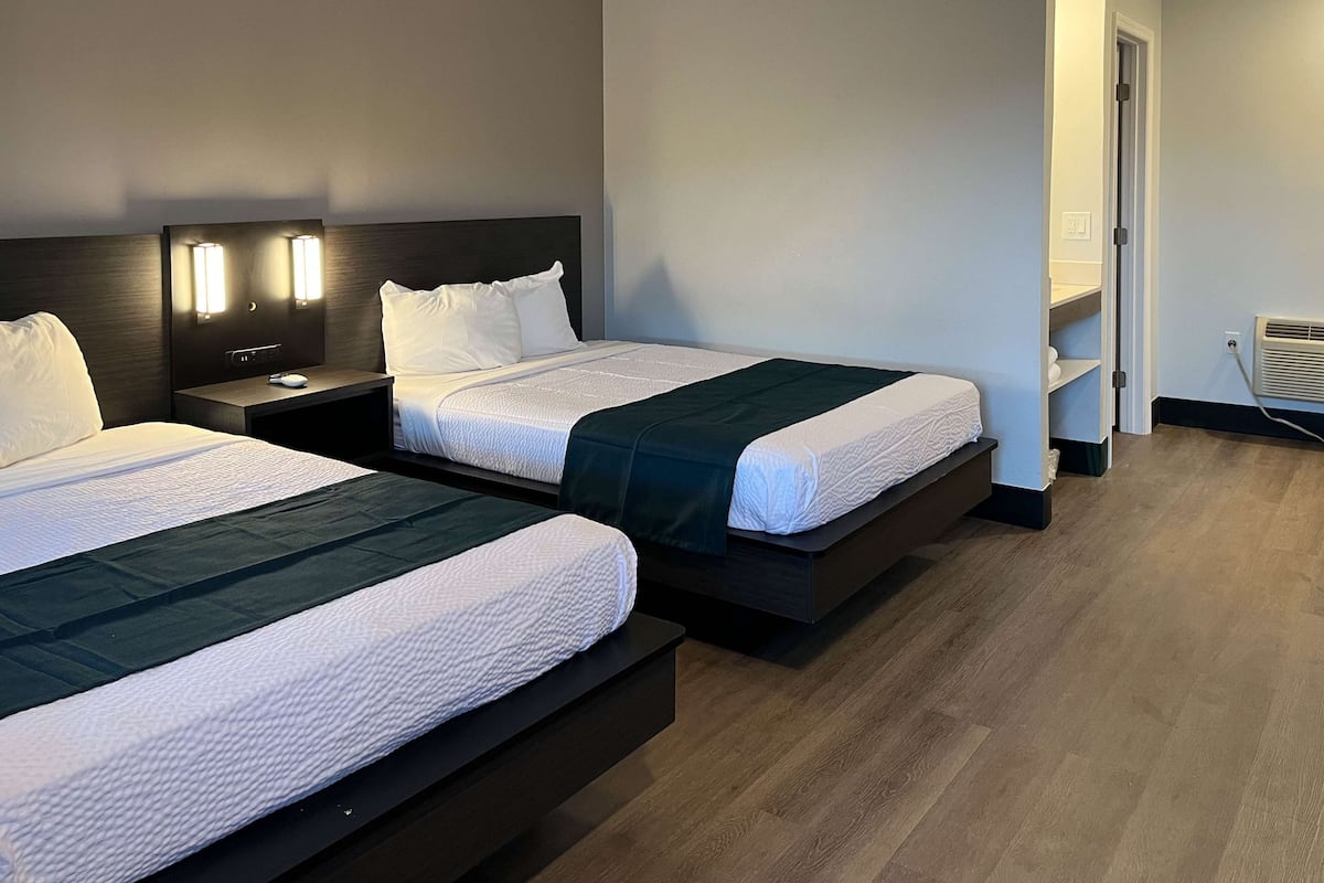 Habitación de hotel con dos camas, una mesita de noche, una lámpara de pared y estante empotrado.
