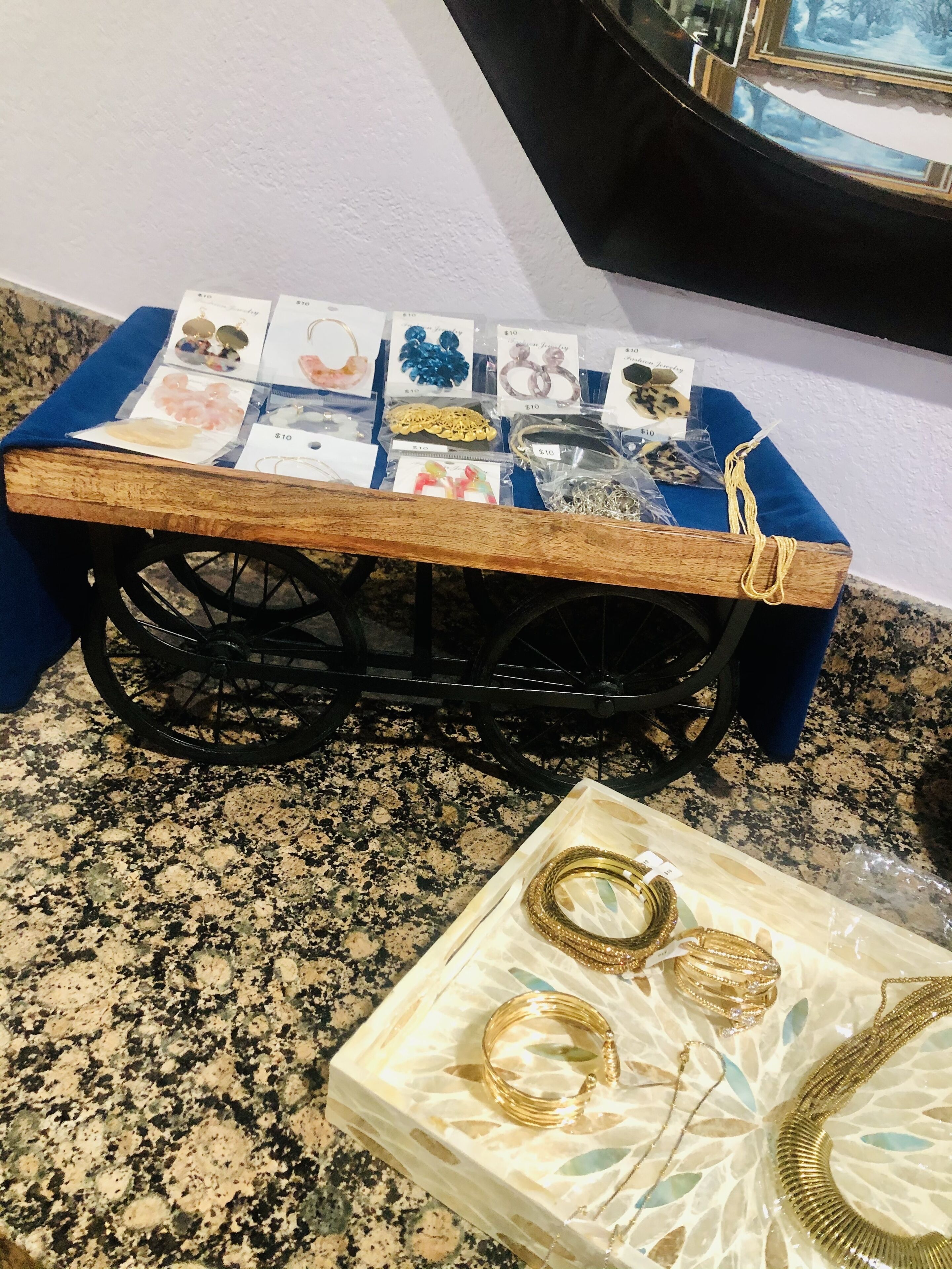 A jewelry display cart with various items priced at $10, including bracelets, necklaces, and earrings, on a granite countertop.