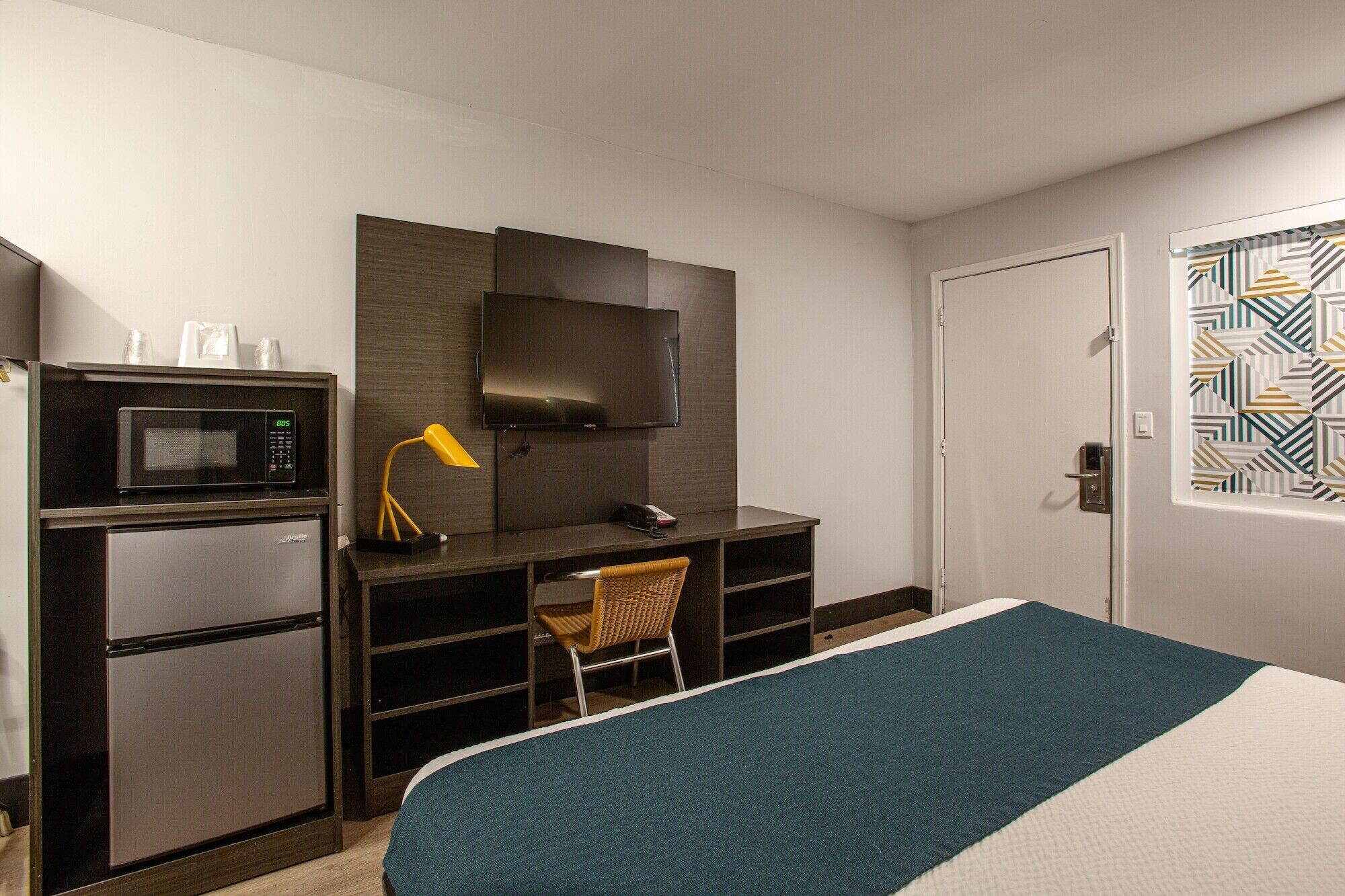 A hotel room with a bed, a desk with a TV, a microwave, and a chair.