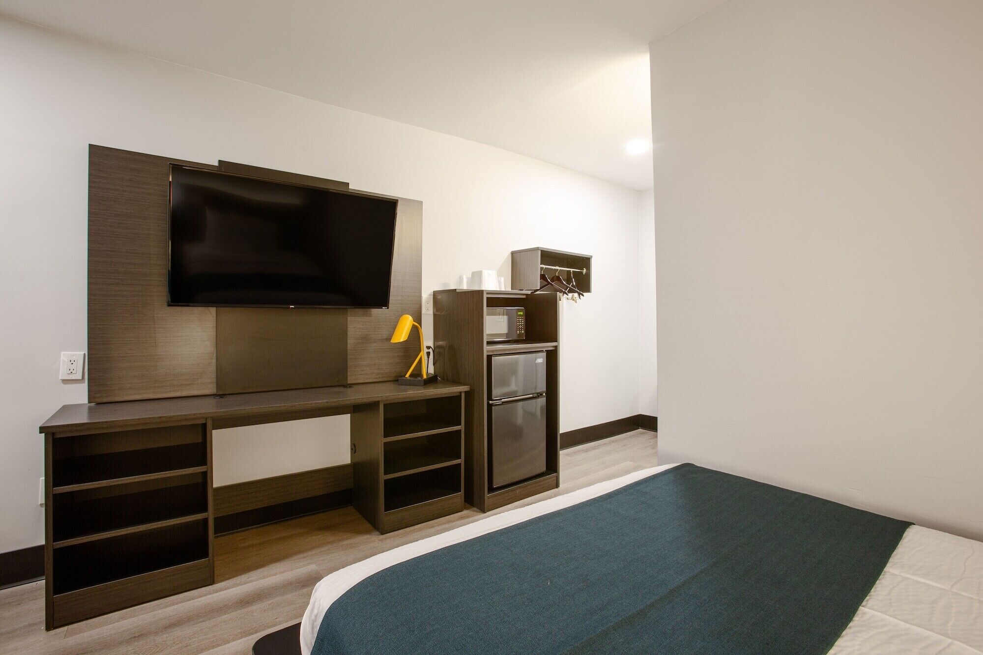Une chambre d’hôtel dotée d’un téléviseur à écran plat fixé au mur, d’une petite kitchenette équipée d’un four à micro-ondes et d’un réfrigérateur, et d’un lit recouvert d’une courtepointe verte et blanche.