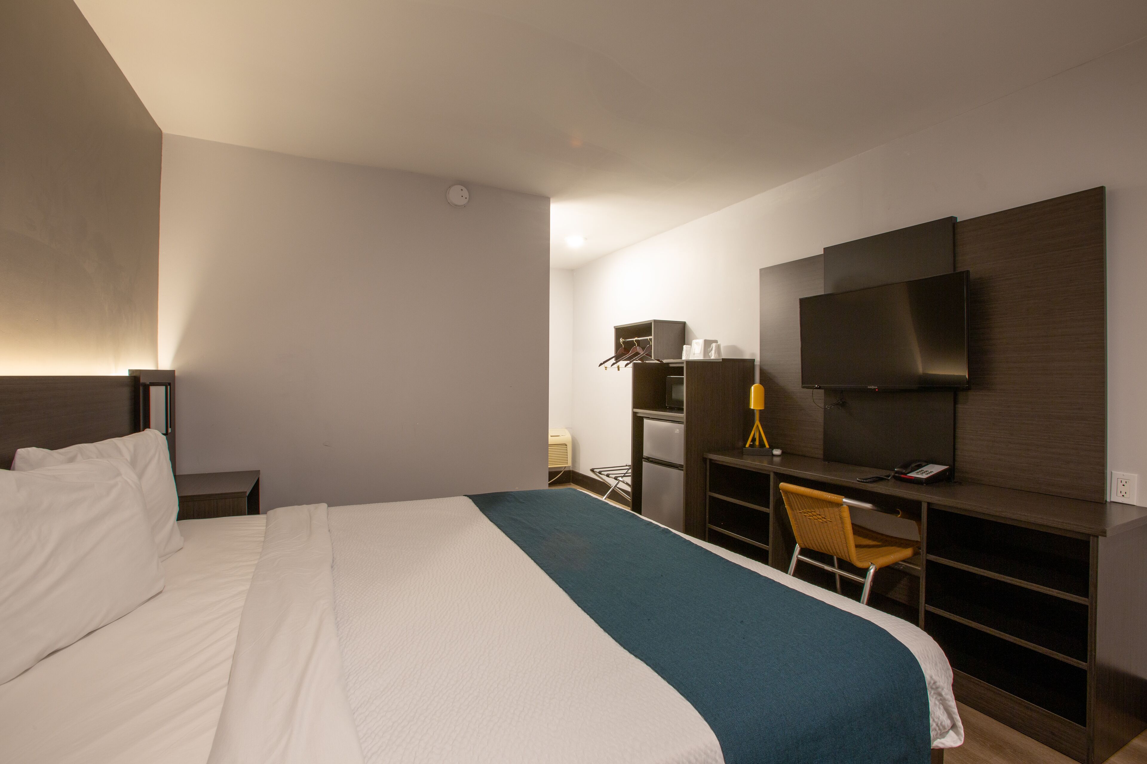 A hotel room with a large bed, a desk with a chair, a television, and a wardrobe.