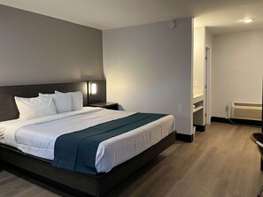 A modern hotel room with a large bed, a bedside table with a lamp, a built-in heater, and a small seating area with a chair. - Motel 6 Williams, AZ - Downtown - Grand Canyon (Williams)