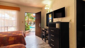 A hotel room with two beds, a desk, a TV, and a view of a pool and palm trees. - Azteca Inn (Mazatlán)