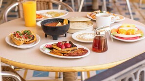 A breakfast table with various dishes, including toast, pancakes, and fruit. - Azteca Inn (Mazatlán)