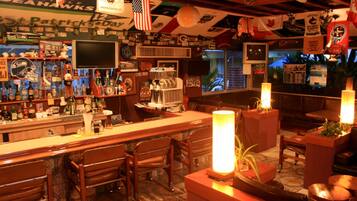 Zona de bar con mobiliario de madera, un televisor y varias decoraciones, incluyendo banderas y recuerdos deportivos.