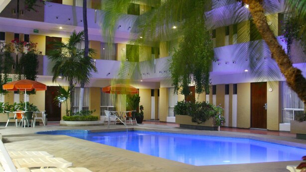 A hotel pool area with multiple lounge chairs, palm trees, and umbrellas. - Azteca Inn (Mazatlán)