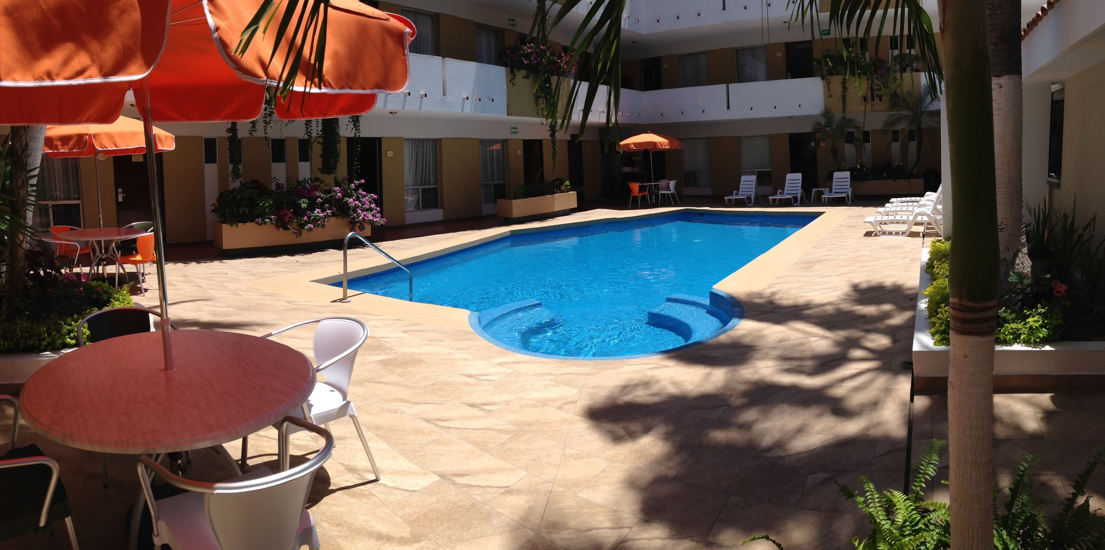 Ein Pool mit Liegestühlen und Tischen, umgeben von Kübelpflanzen und Sonnenschirmen.