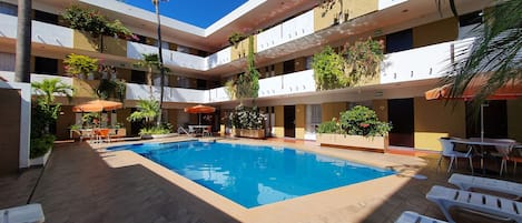 A multi-level hotel with a central swimming pool, outdoor seating, and balconies with plants.
