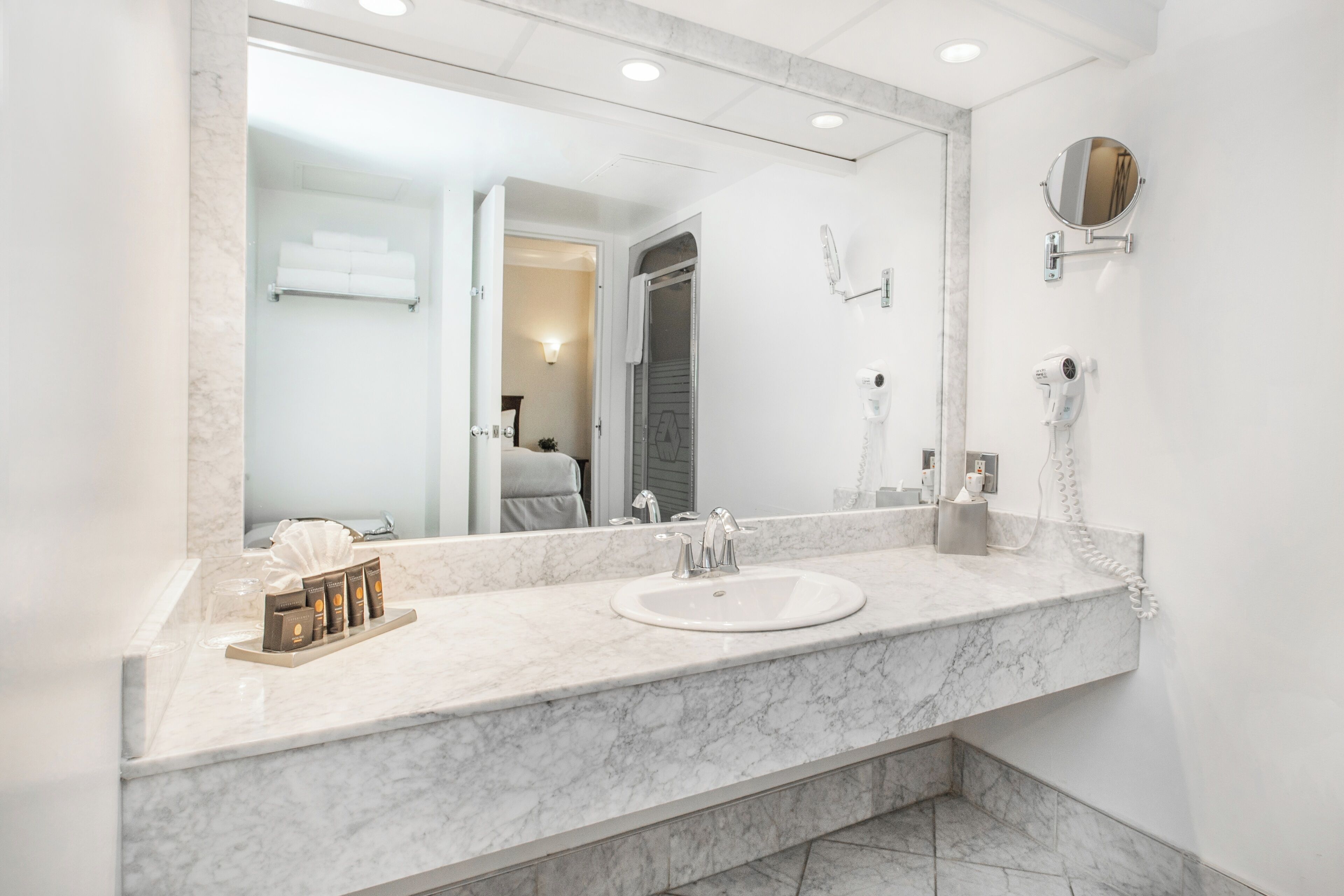 A bathroom with a marble sink, a large mirror, a hairdryer, and a towel rack.