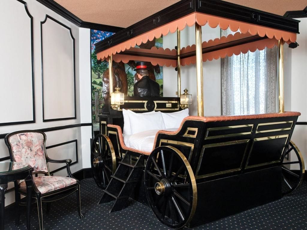 A four-poster bed with a canopy, a chair, and a mirror reflecting a person.