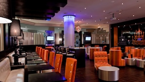 Un hall d’hôtel moderne, doté d’espaces aménagés avec des sièges, d’un bar et d’une grande colonne illuminée de lumière bleue.