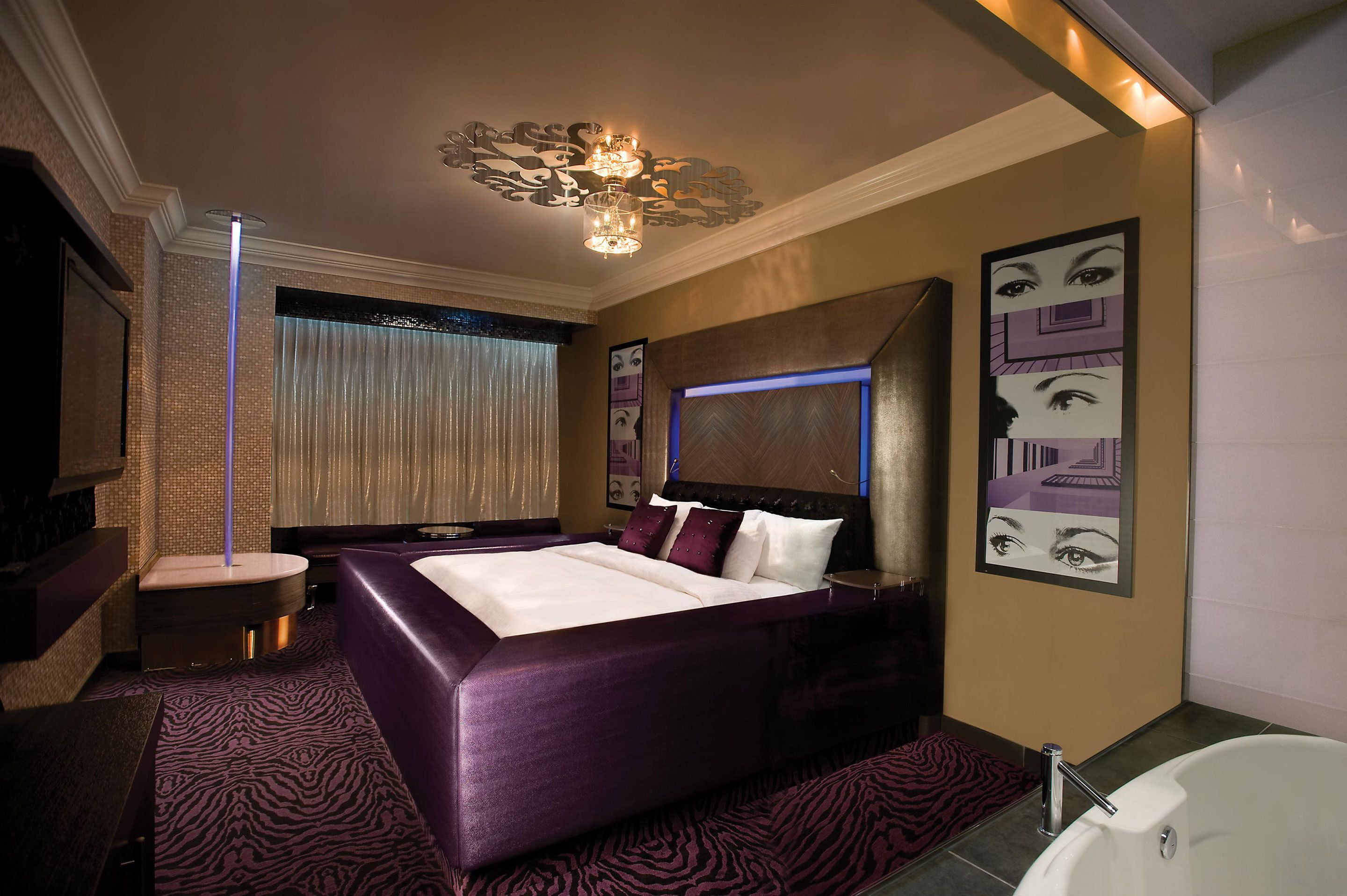 Una habitación de hotel moderna con una cama grande, una zona de estar separada, una bañera y un amplio ventanal con cortinas.
