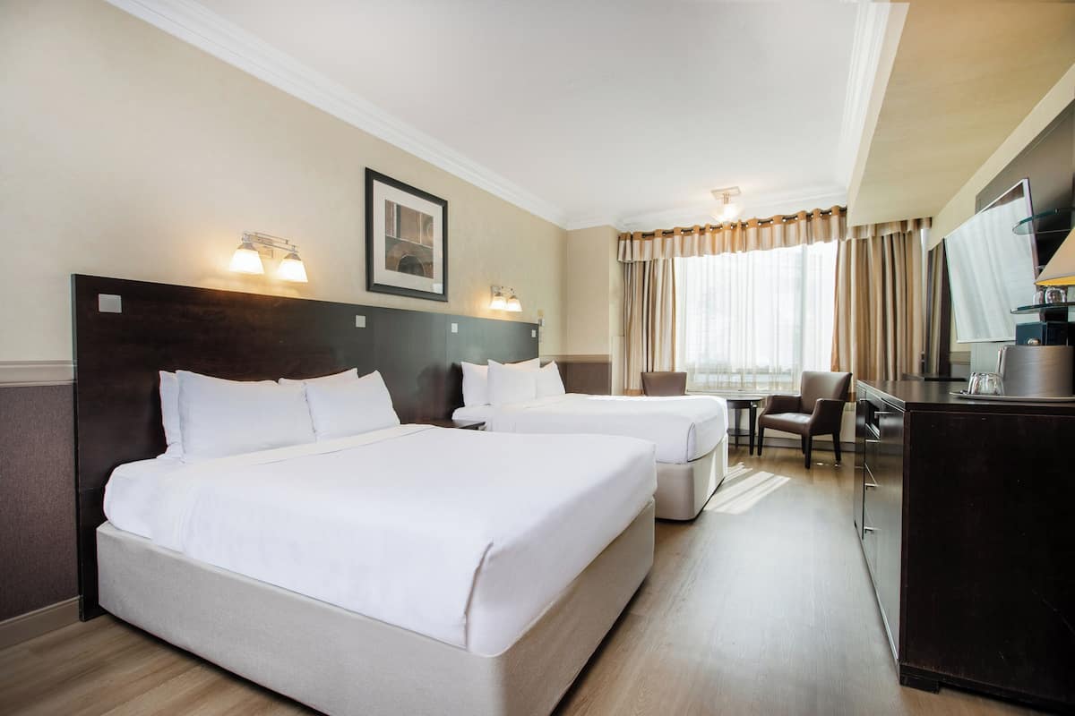 A hotel room with two beds, a desk, a chair, and a large window with curtains.