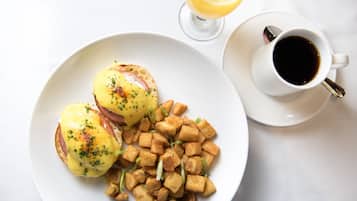 A plate with eggs benedict and fried potatoes, a glass of orange juice, and a cup of coffee on a white table.