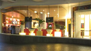 Un hall d’entrée lumineux, doté d’un mur incurvé en verre, d’un bar avec des étagères remplies de bouteilles et de plantes en pot.