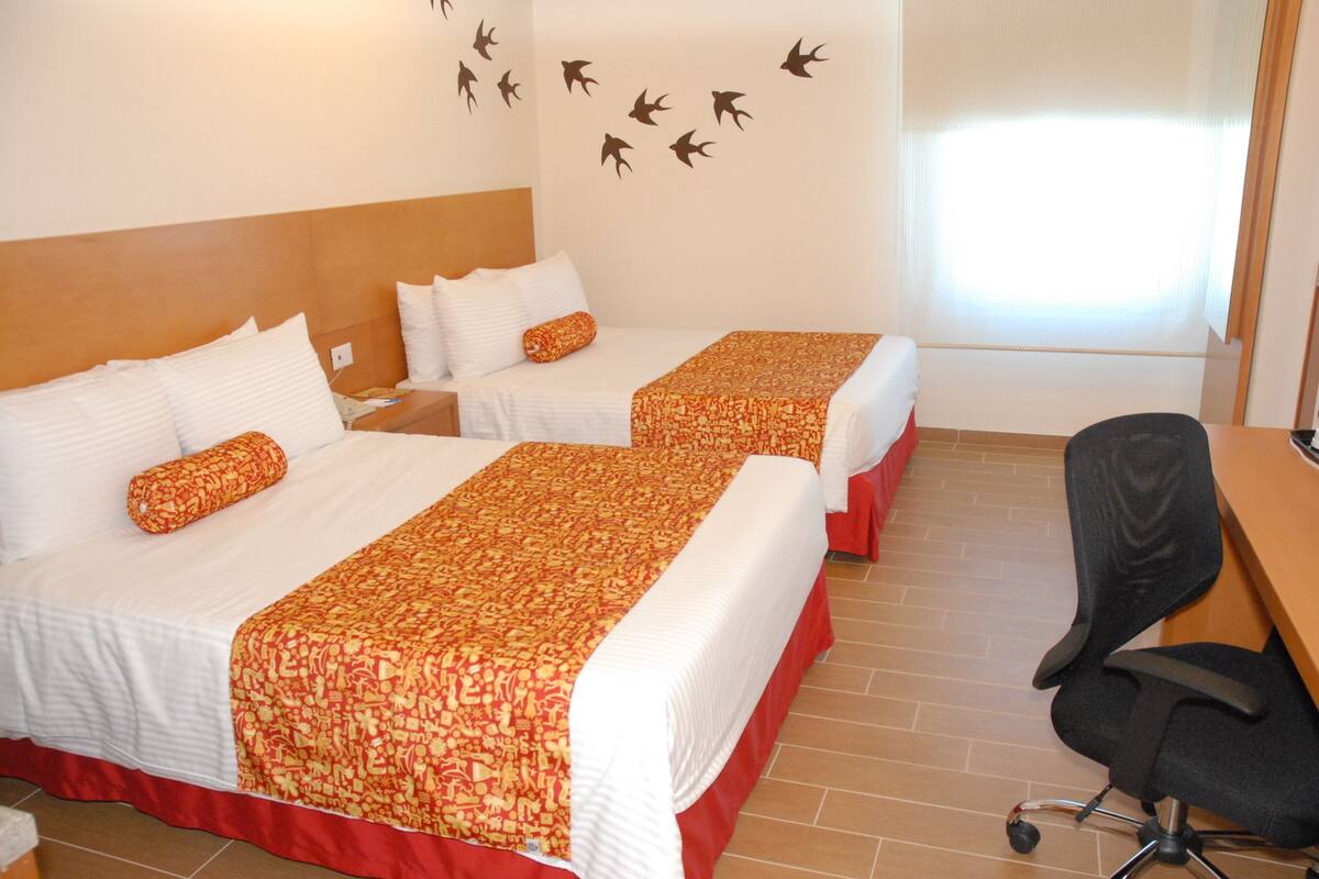 Habitación de hotel con dos camas, un escritorio y una silla.