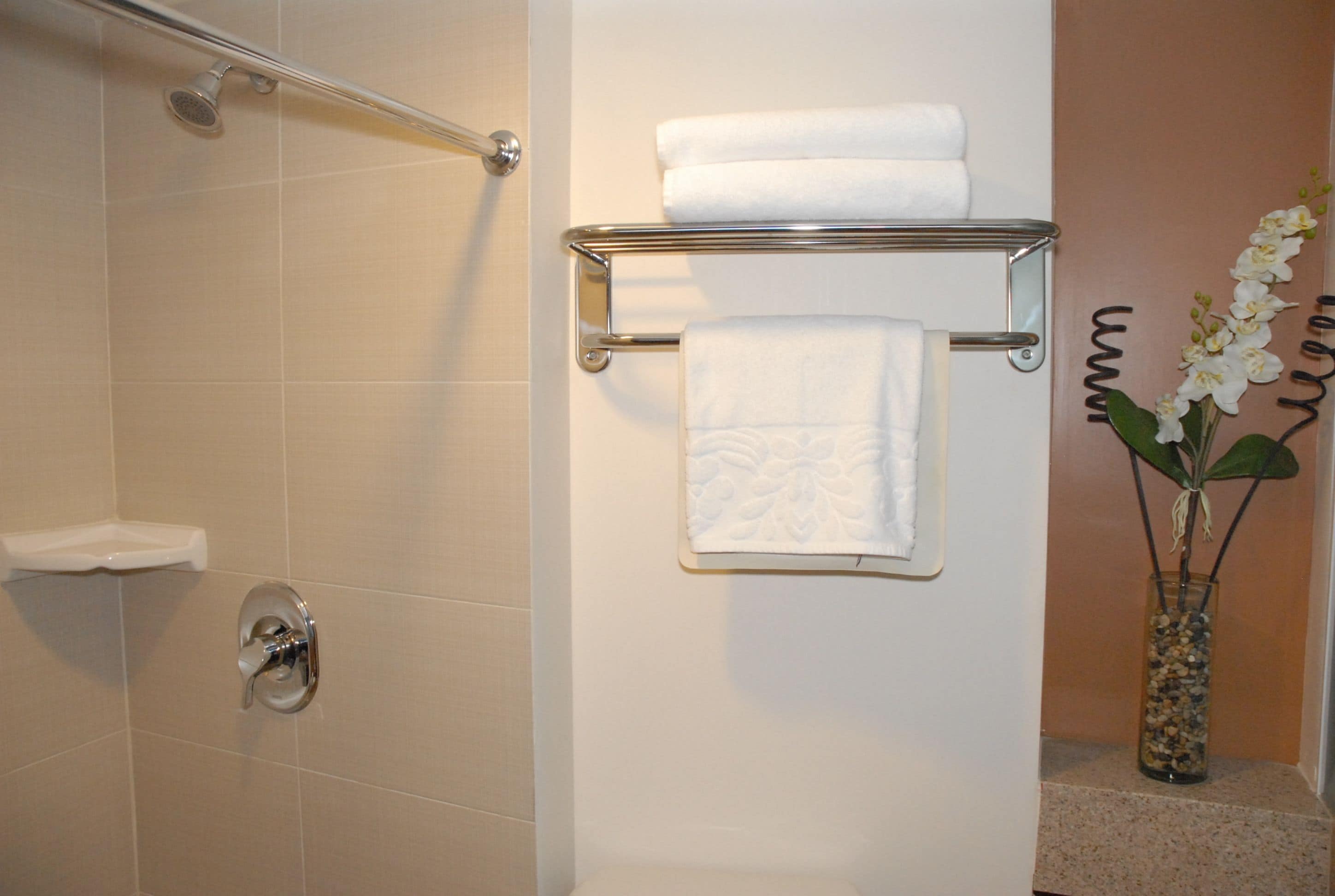 Een badkamer met een douche, een handdoekrek met twee handdoeken en een vaas met bloemen.