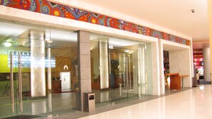Un hall d’hôtel moderne avec des portes vitrées, un comptoir d’accueil et une fresque colorée sur le mur.