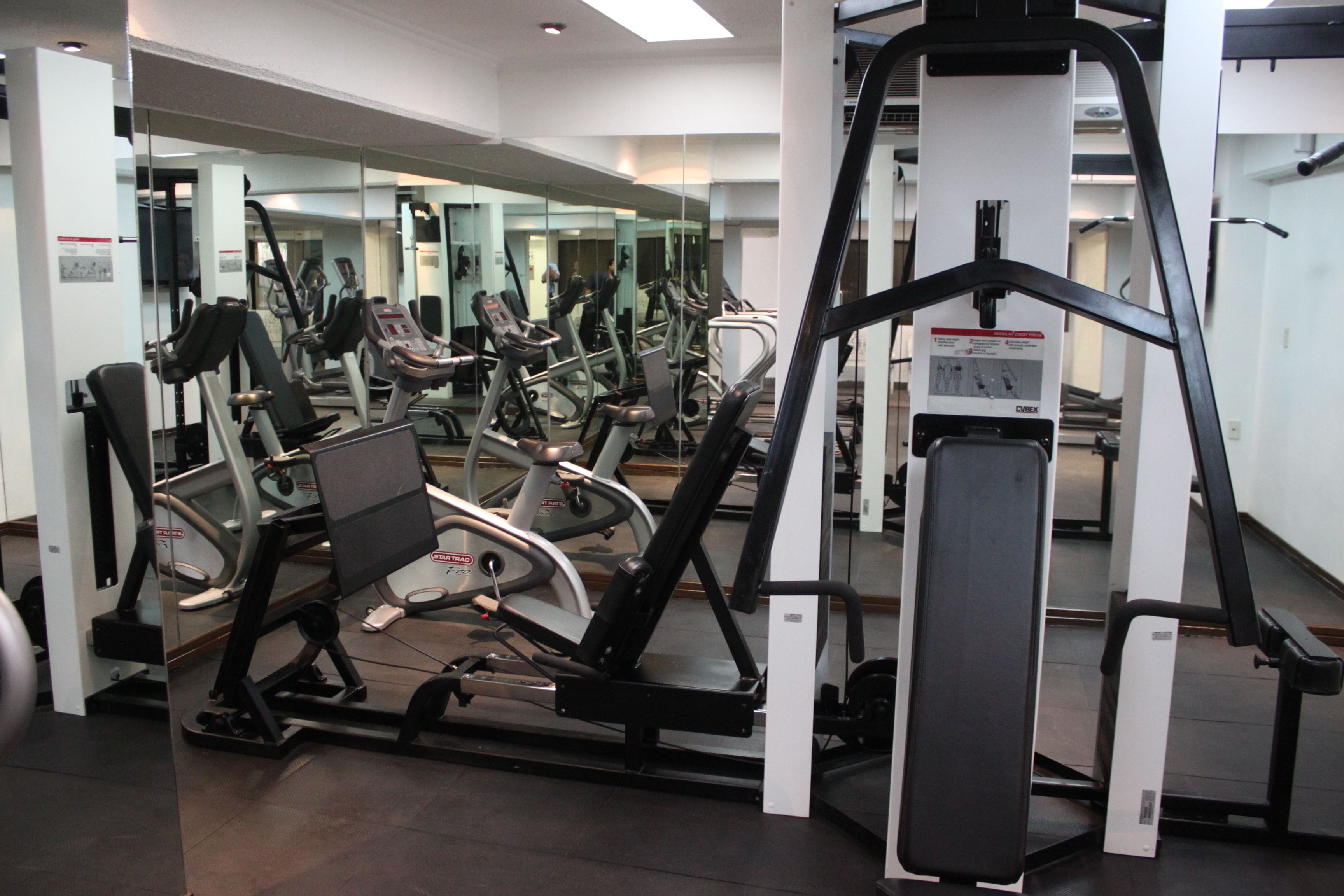 Un gimnasio con varias máquinas de ejercicio, espejos y un diseño moderno y limpio.