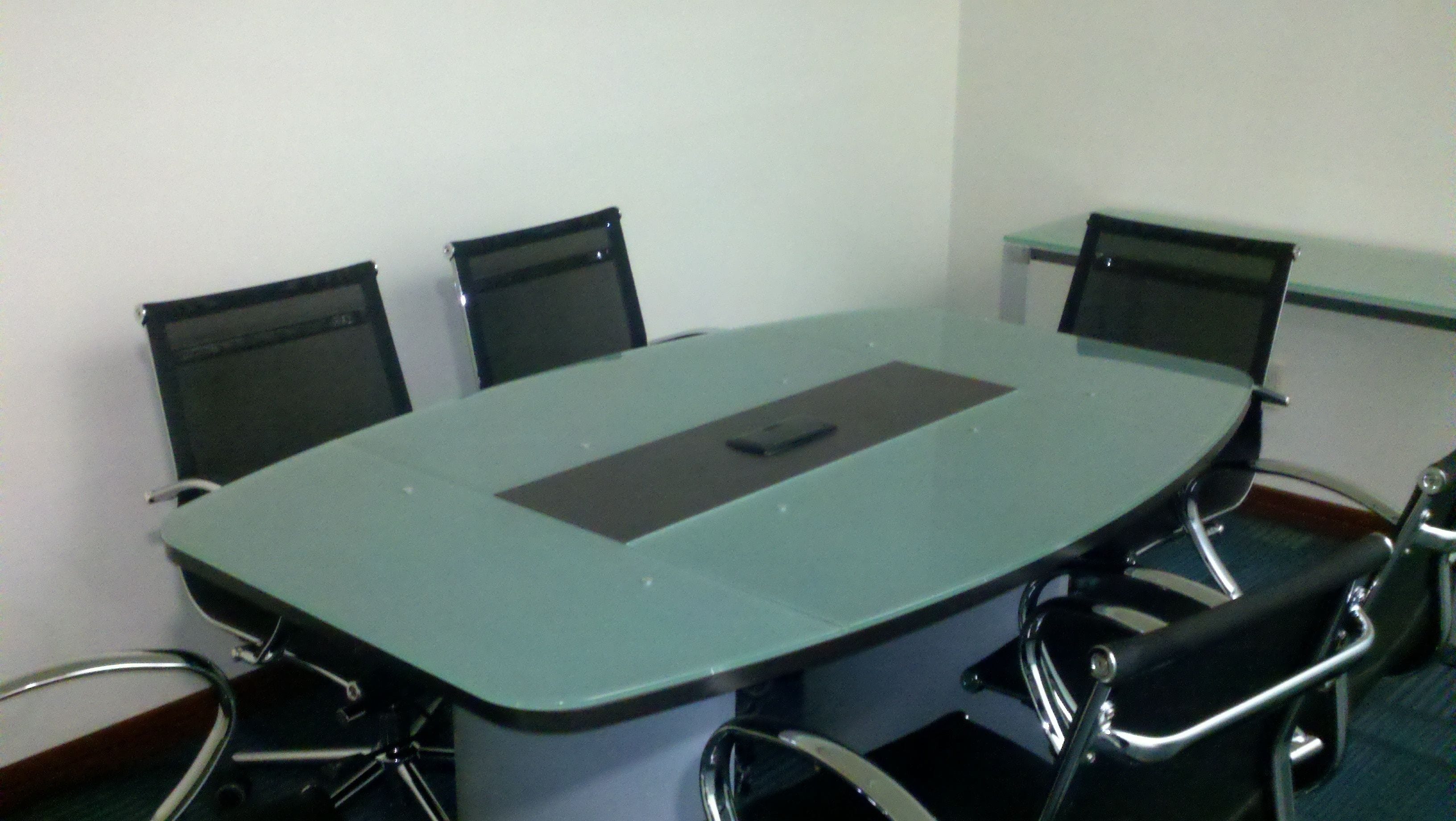 A conference room with a glass table, four chairs, and a projector.