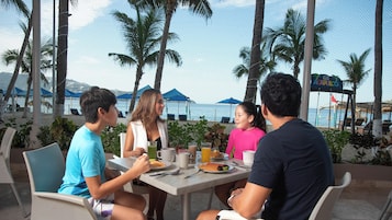 Un grupo de personas cenando en una mesa al aire libre con vista a la playa y al océano.