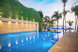 Una piscina con un muro verde y palmeras al fondo.