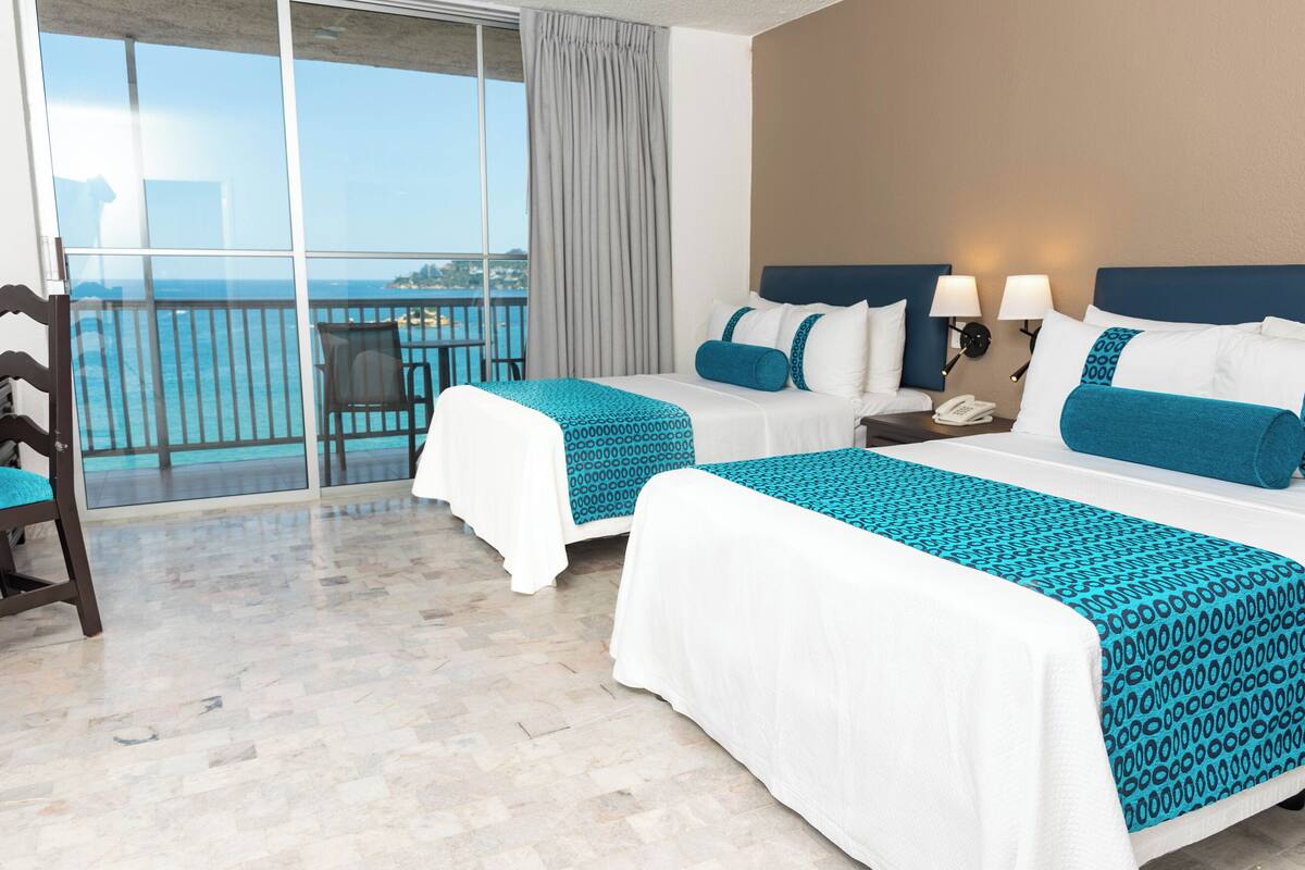 A hotel room with two beds, a balcony with a view, a chair, and a nightstand with a phone.