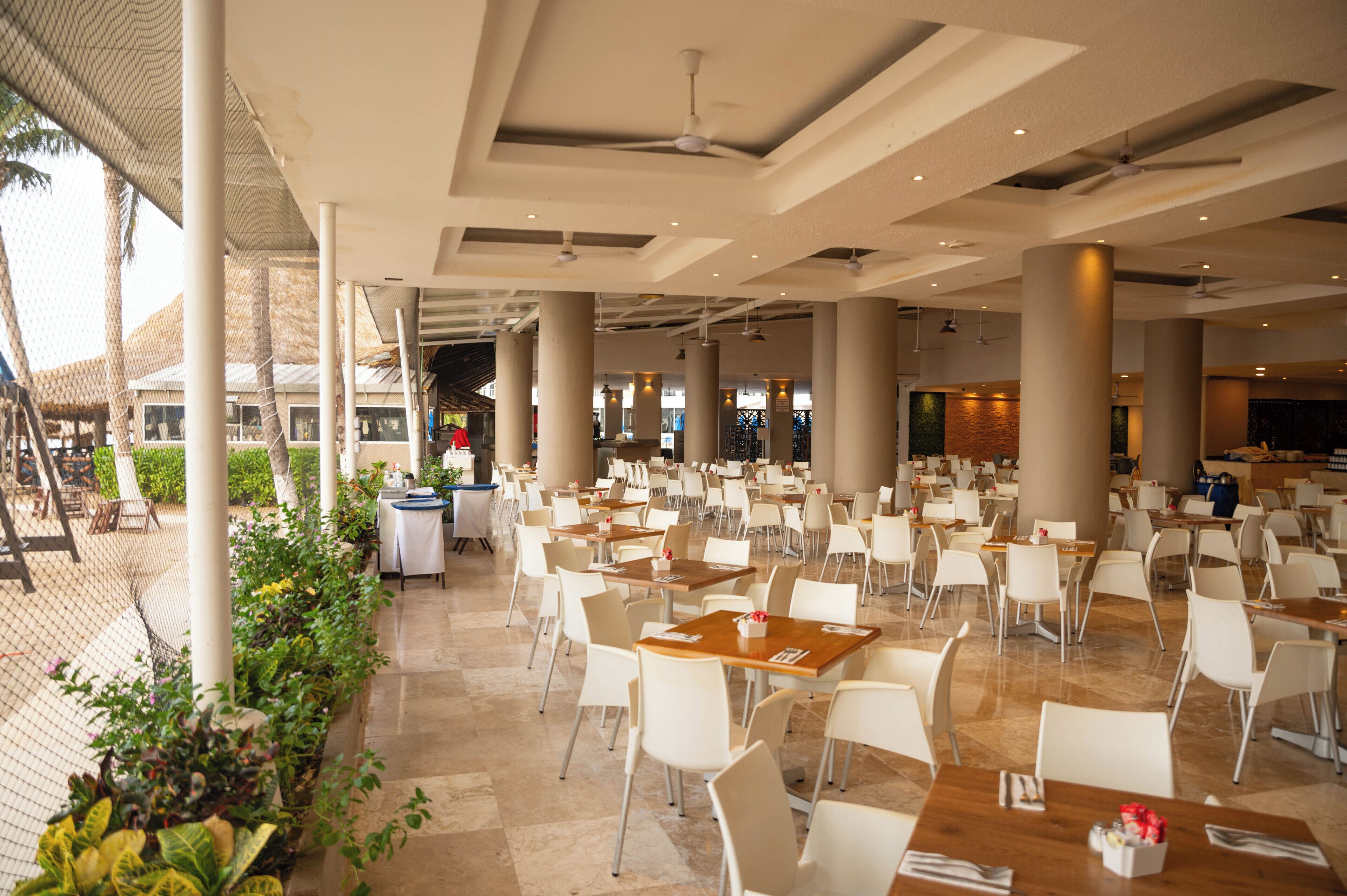 A spacious indoor dining area with multiple tables and chairs, large pillars, and ceiling fans.