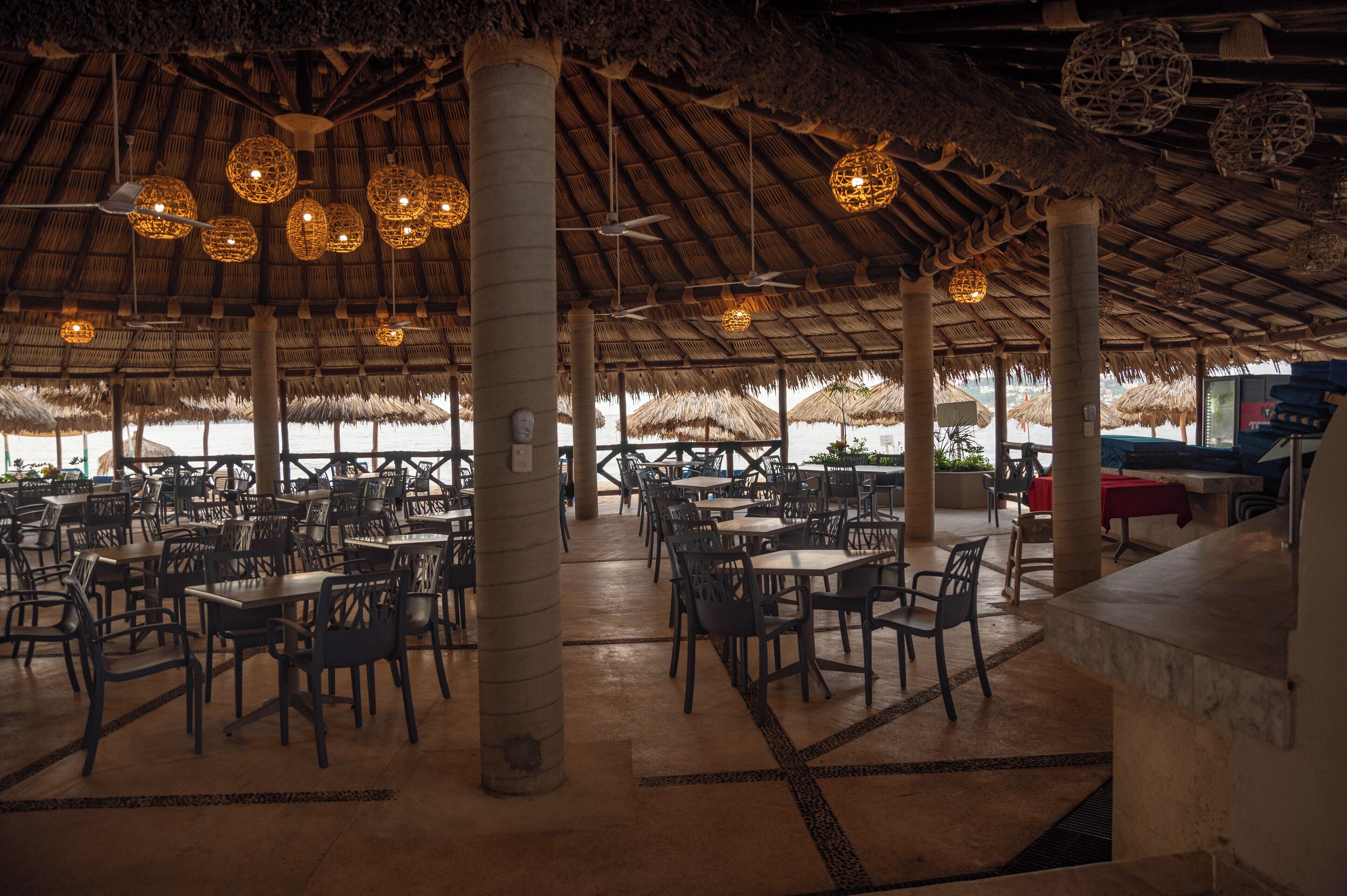 Un comedor interior con techos de paja, mesas y sillas dispuestas para los huéspedes.