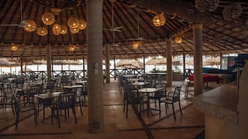 Un comedor interior con techos de paja, mesas y sillas dispuestas para los huéspedes.