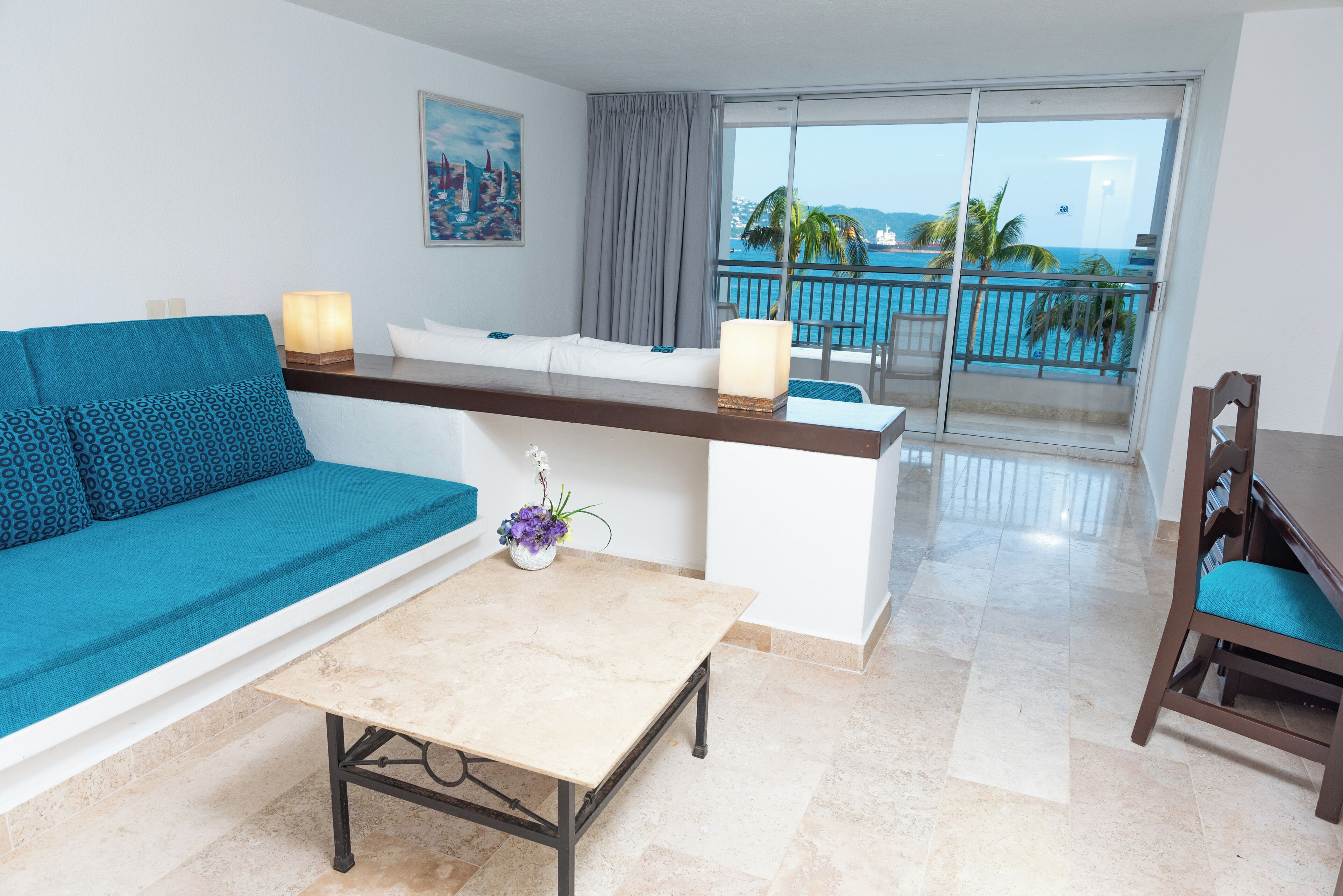 A modern hotel room with a balcony, a sofa, a table, and a chair.