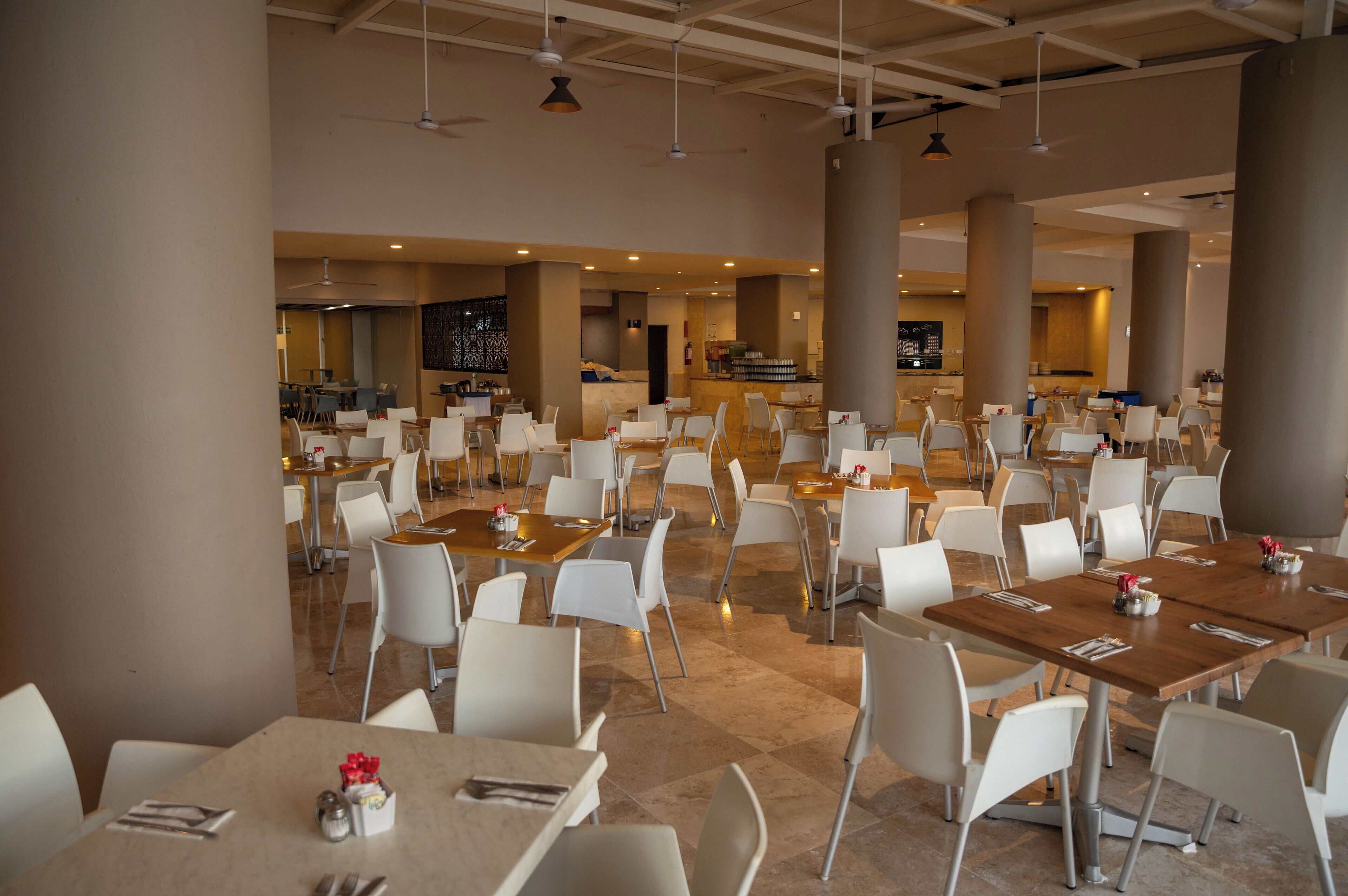 A spacious dining area with multiple tables and chairs, large pillars, and a modern ceiling design.