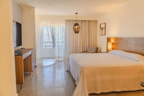 A hotel room with a bed, a desk, a chair, a television, and a window with curtains. - Friendly Fun Vallarta Different Experiences (Puerto Vallarta)