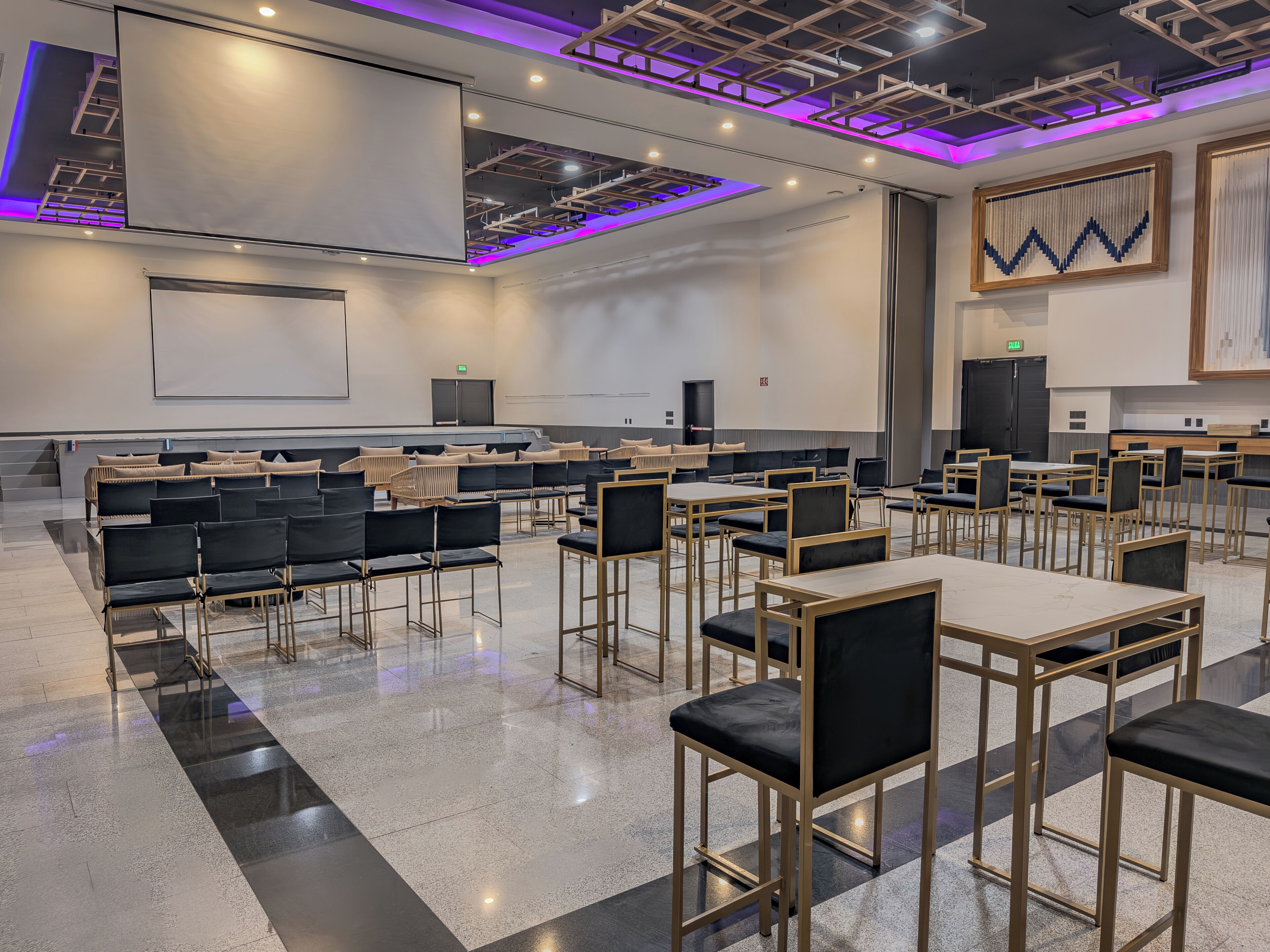 A conference room with rows of chairs and tables, a large screen, and a modern ceiling design.