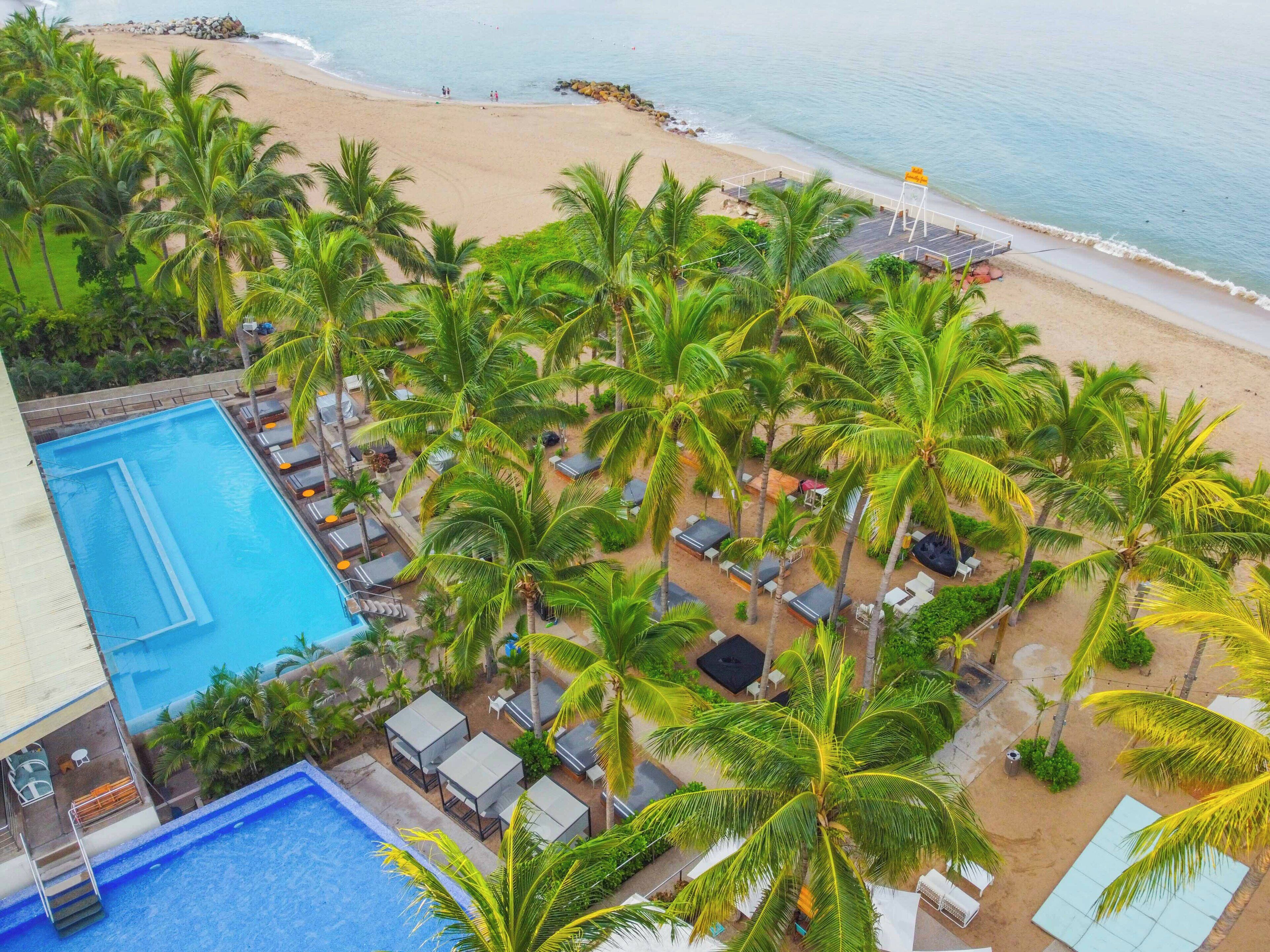A resort with a swimming pool, beach, and palm trees.