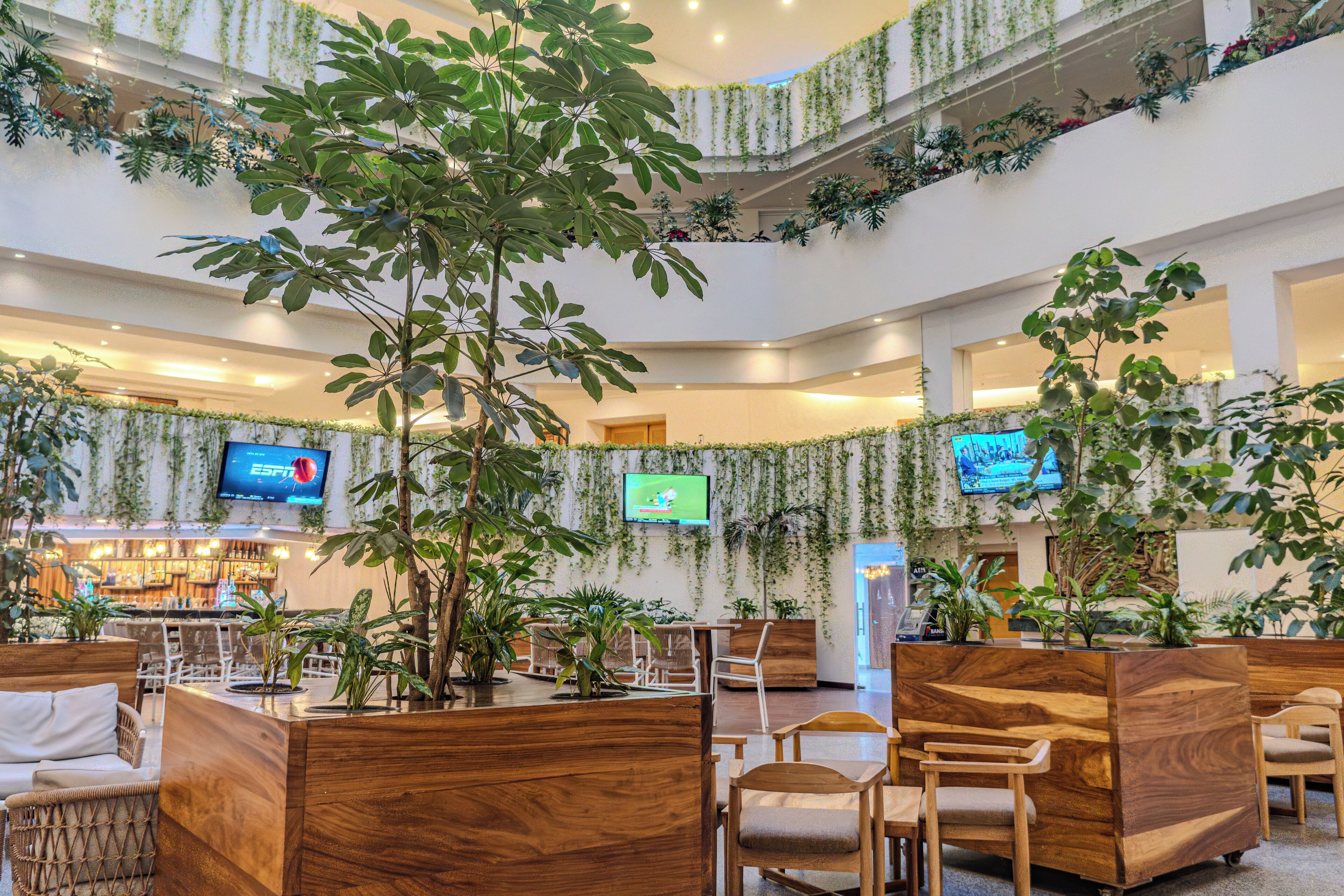 A multi-level lobby with wooden seating, potted plants, and a bar area.