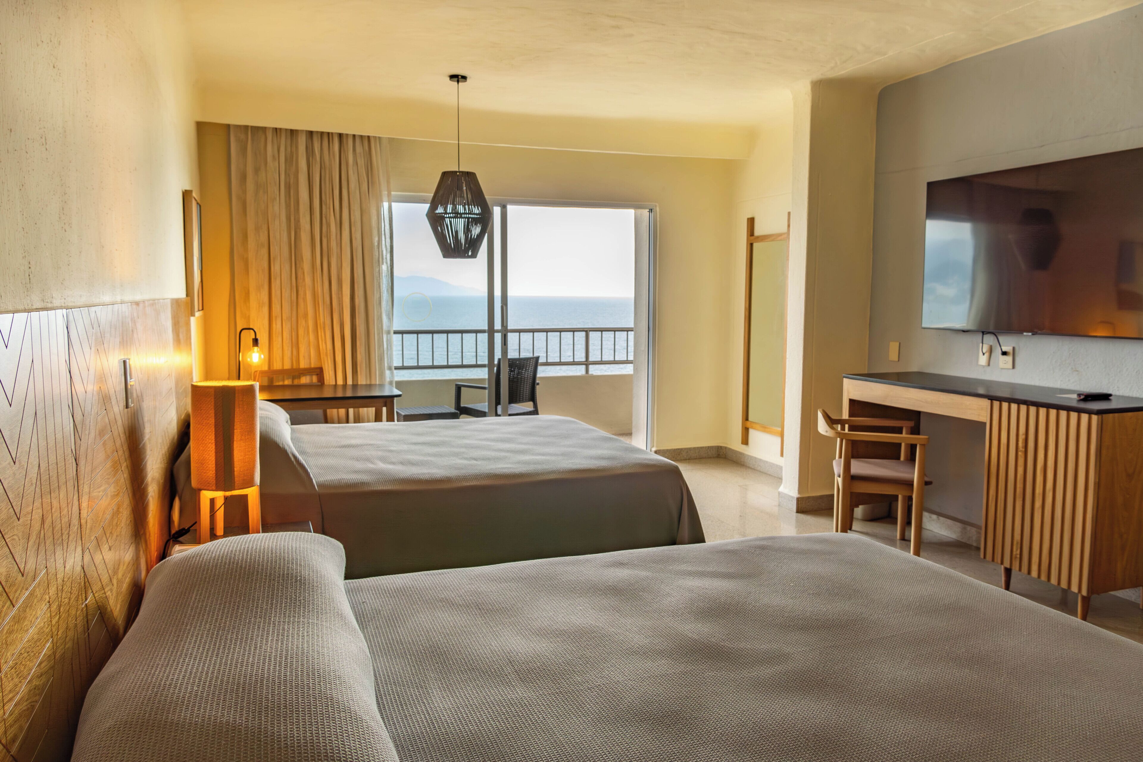 Habitación de hotel con dos camas, un escritorio, una silla, un televisor y vista al mar.