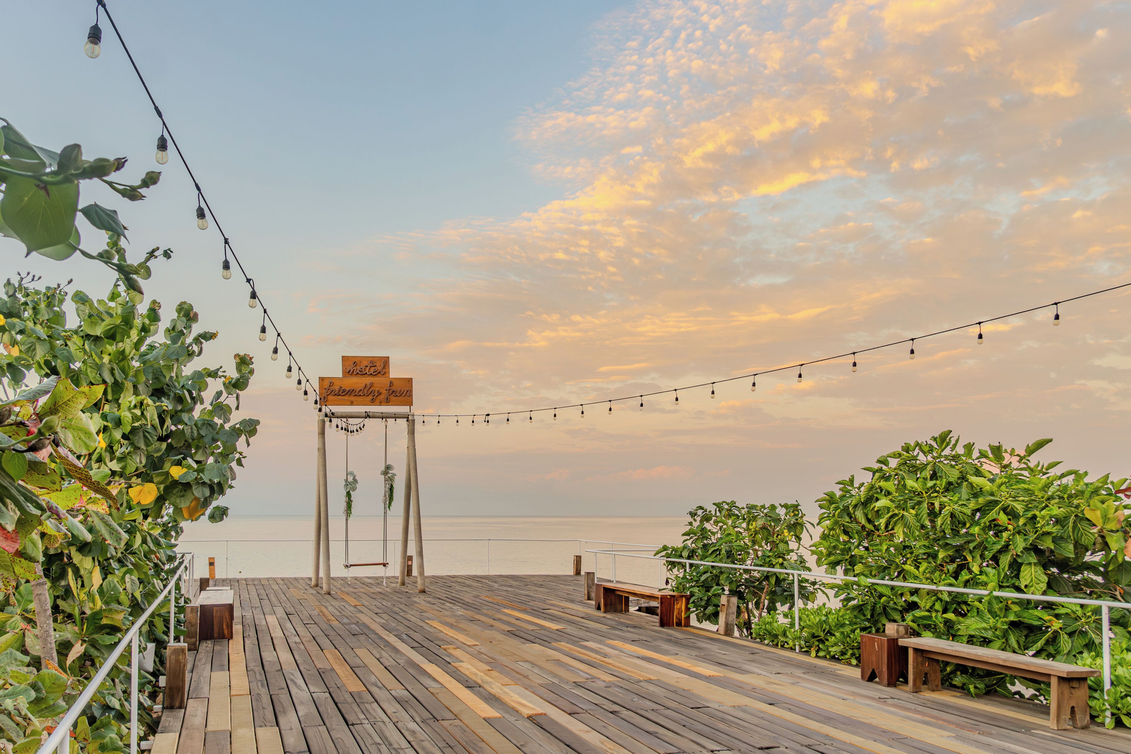 A wooden deck with string lights, a wooden sign, and greenery.