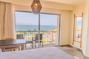 A hotel room with a bed, a table, chairs, a balcony with a view of the sea, and a hanging light fixture. - Friendly Fun Vallarta Different Experiences (Puerto Vallarta)