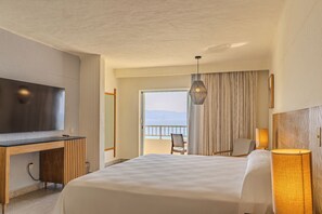 Ein Hotelzimmer mit Bett, Schreibtisch mit Fernseher, Stuhl, Lampe und Meerblick durch ein großes Fenster.