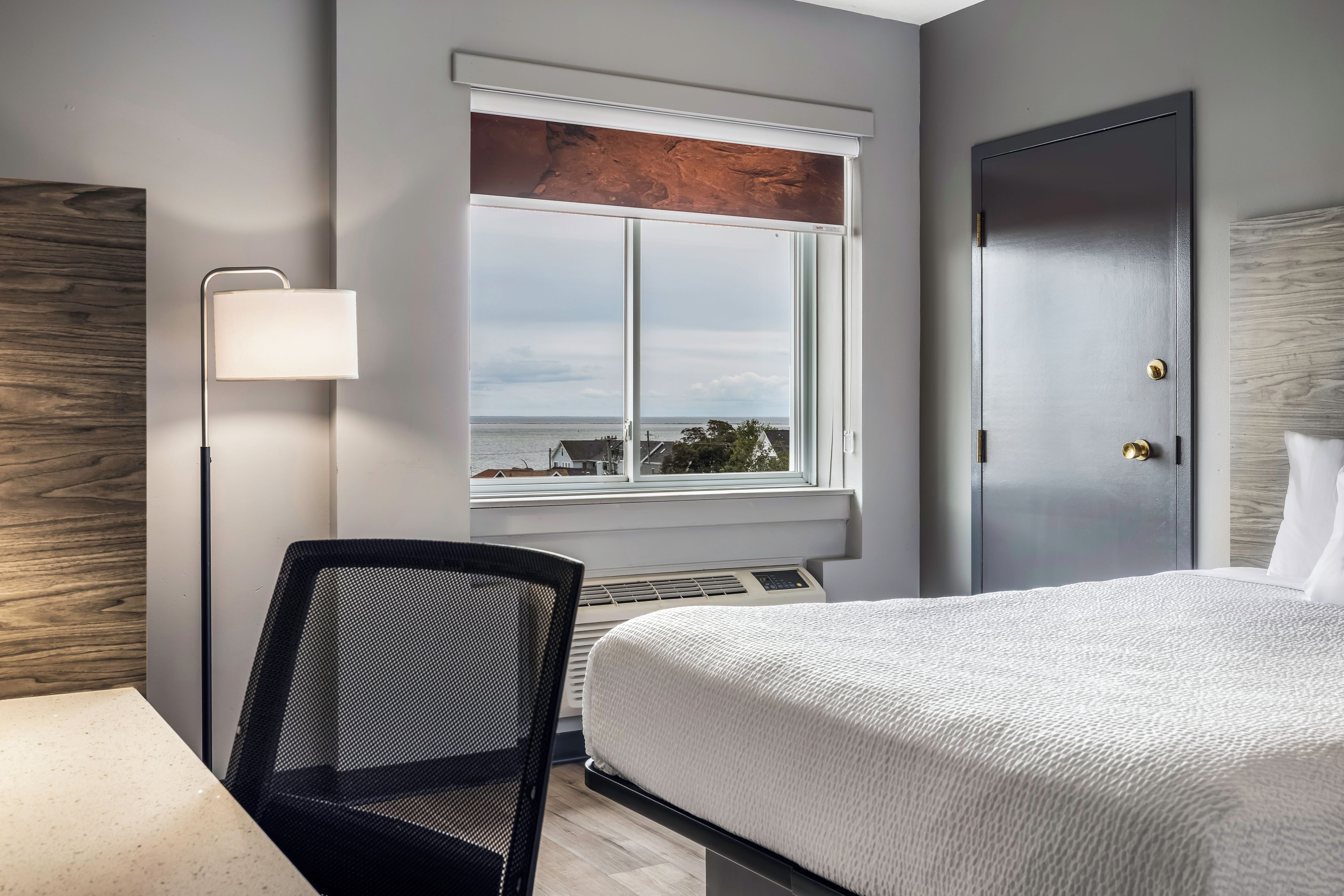 Habitación de hotel con cama, escritorio, silla, ventana con vistas y puerta.