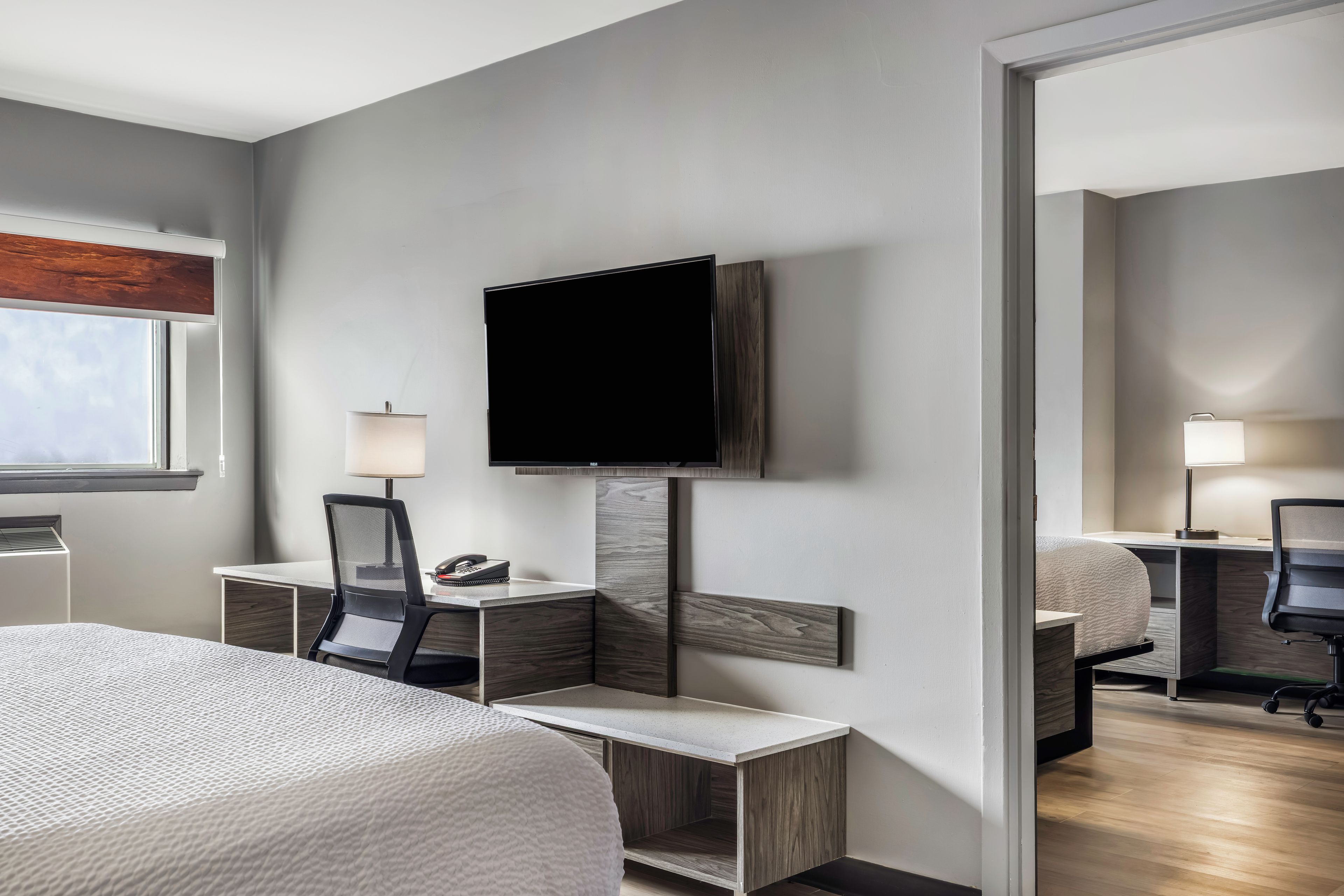 A hotel room with a bed, a desk with a chair, a television, and a mirror.
