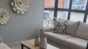A modern living room with a grey brick wall, a beige sofa, a matching armchair, a wooden coffee table with two vases, and large white floral wall decorations. - Days Inn & Suites by Wyndham Summerside (Summerside)