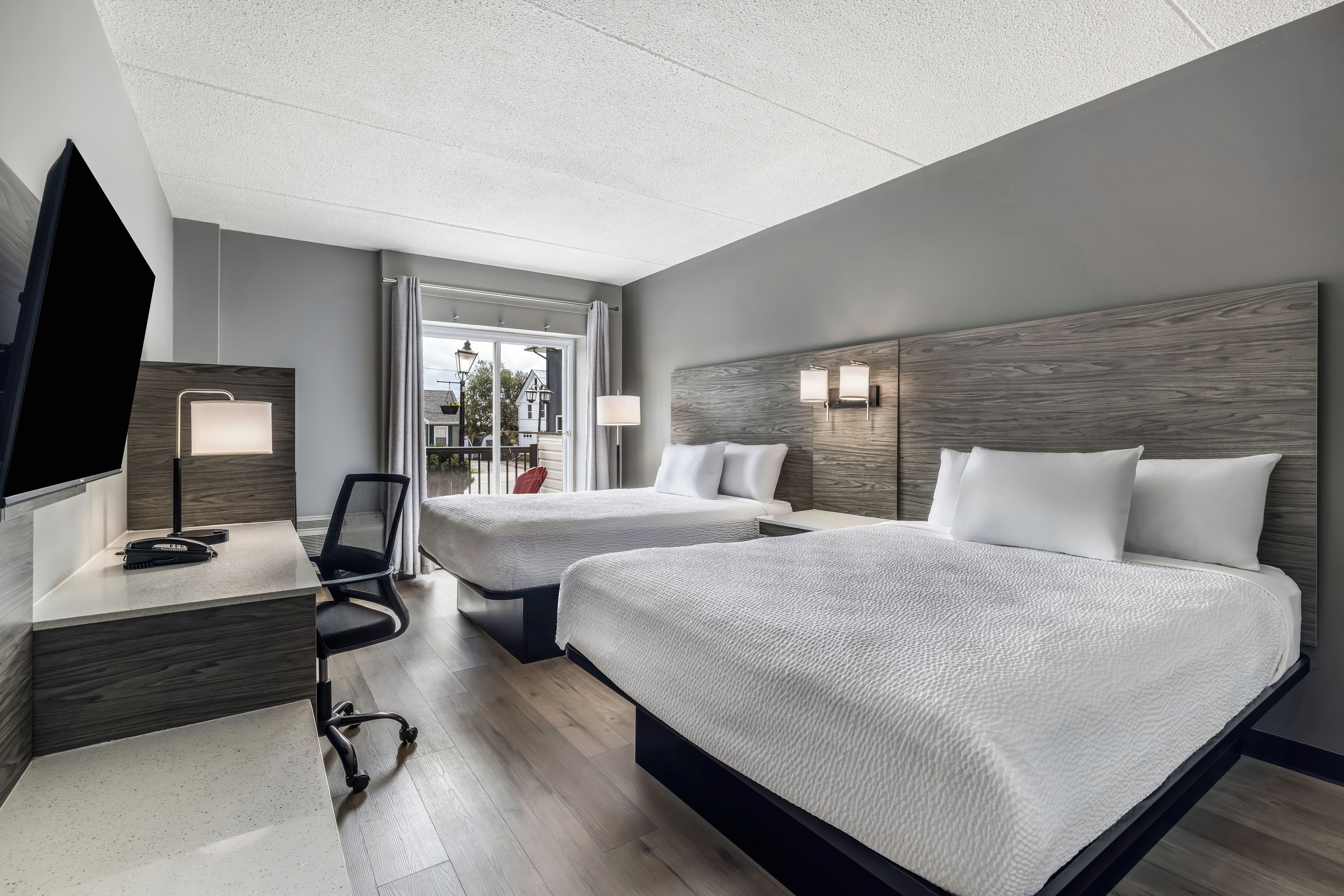 A hotel room with two beds, a desk, a chair, a TV, and a window with curtains.