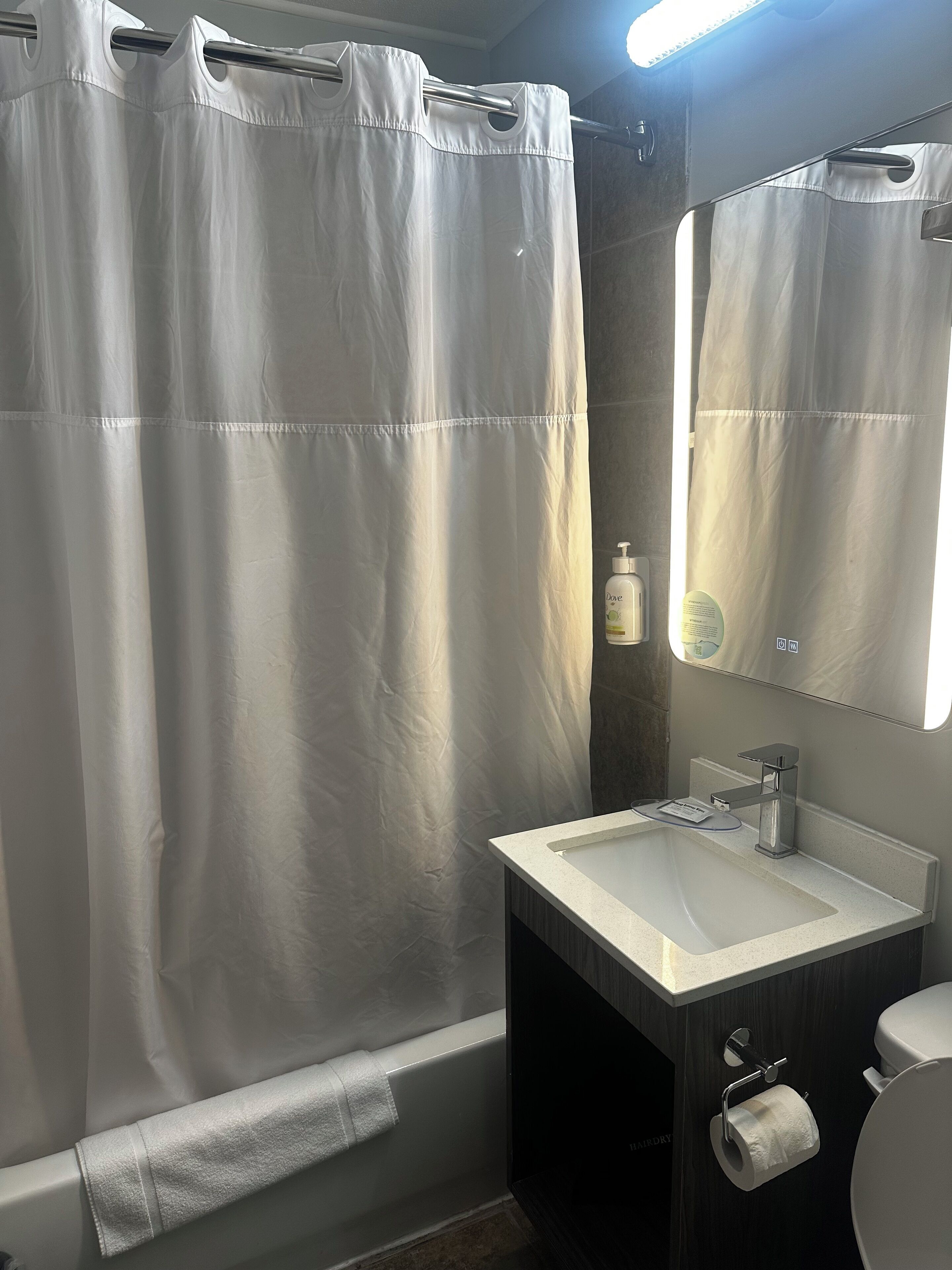 A bathroom with a shower curtain, a sink, a mirror, a towel, and a toilet.