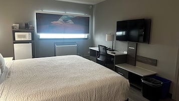 A hotel room with a bed, a desk, a TV, a microwave, and a window.