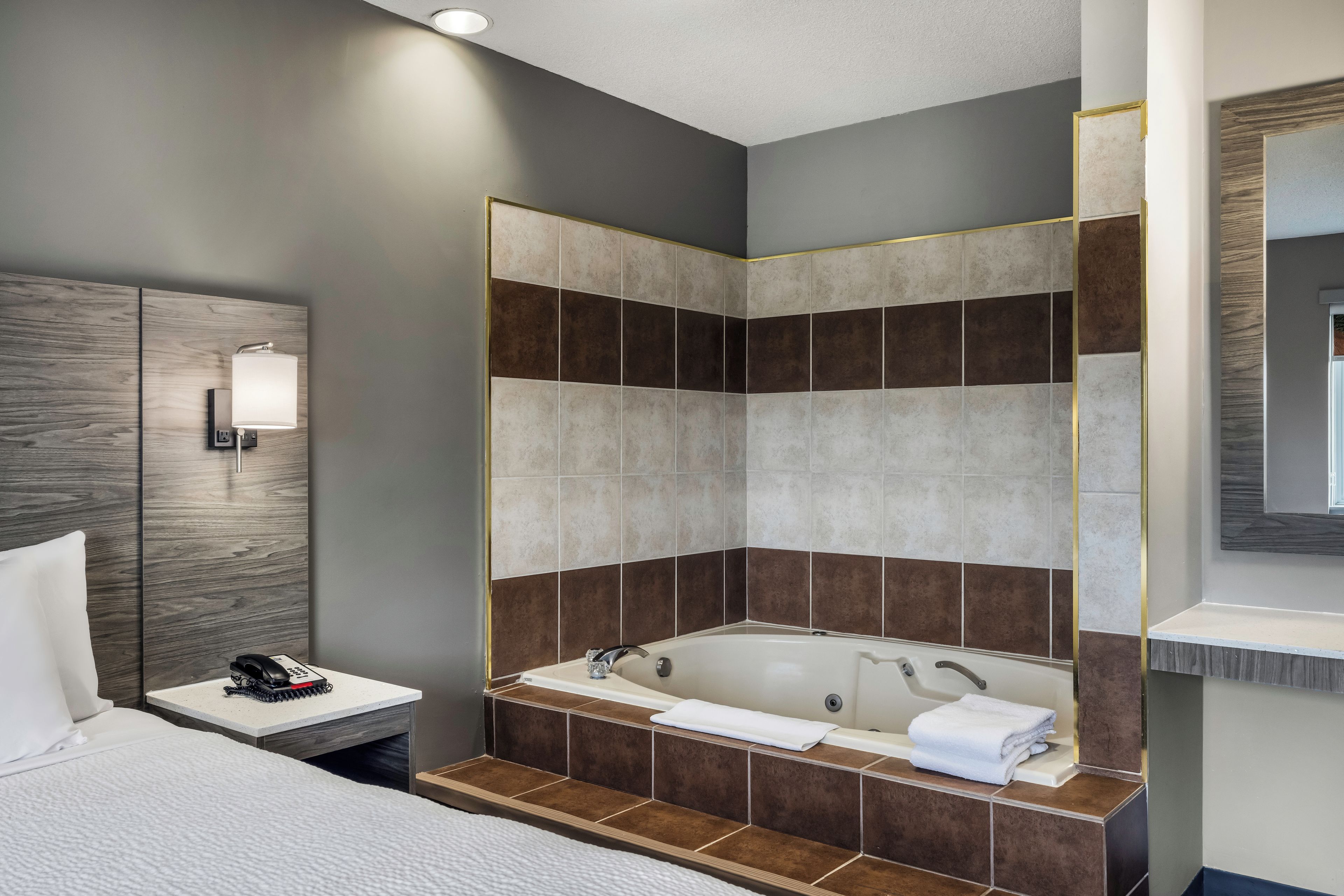 A modern bathroom with a bathtub, a shower area, and a bedside table with a telephone and a notepad.