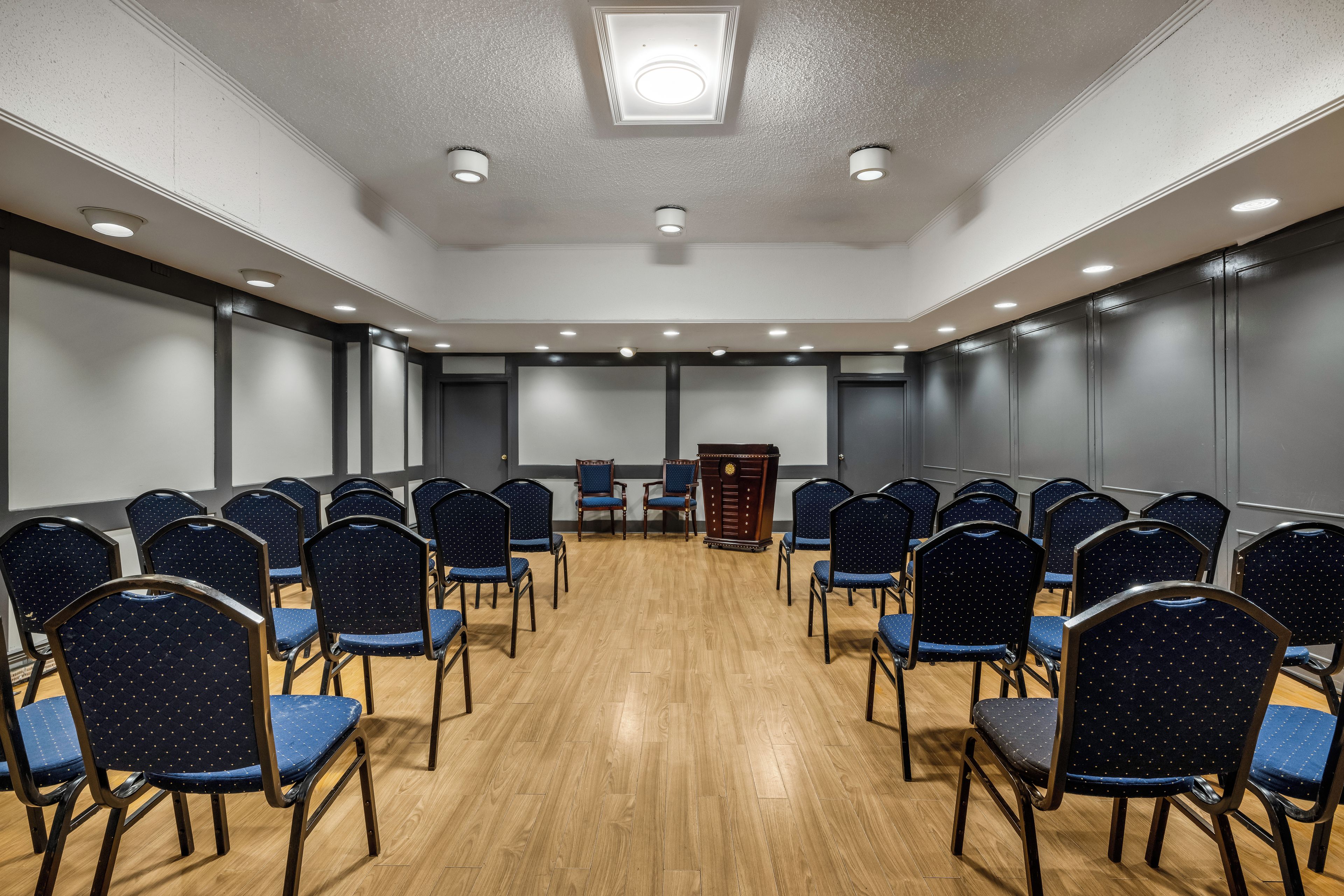 A conference room with rows of chairs, a podium, and a projector screen.