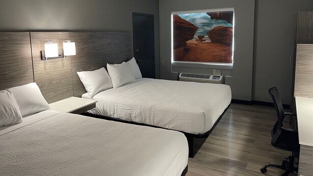 A hotel room with two beds, a desk, a chair, and a large window with a desert landscape view. - Days Inn & Suites by Wyndham Summerside (Summerside)