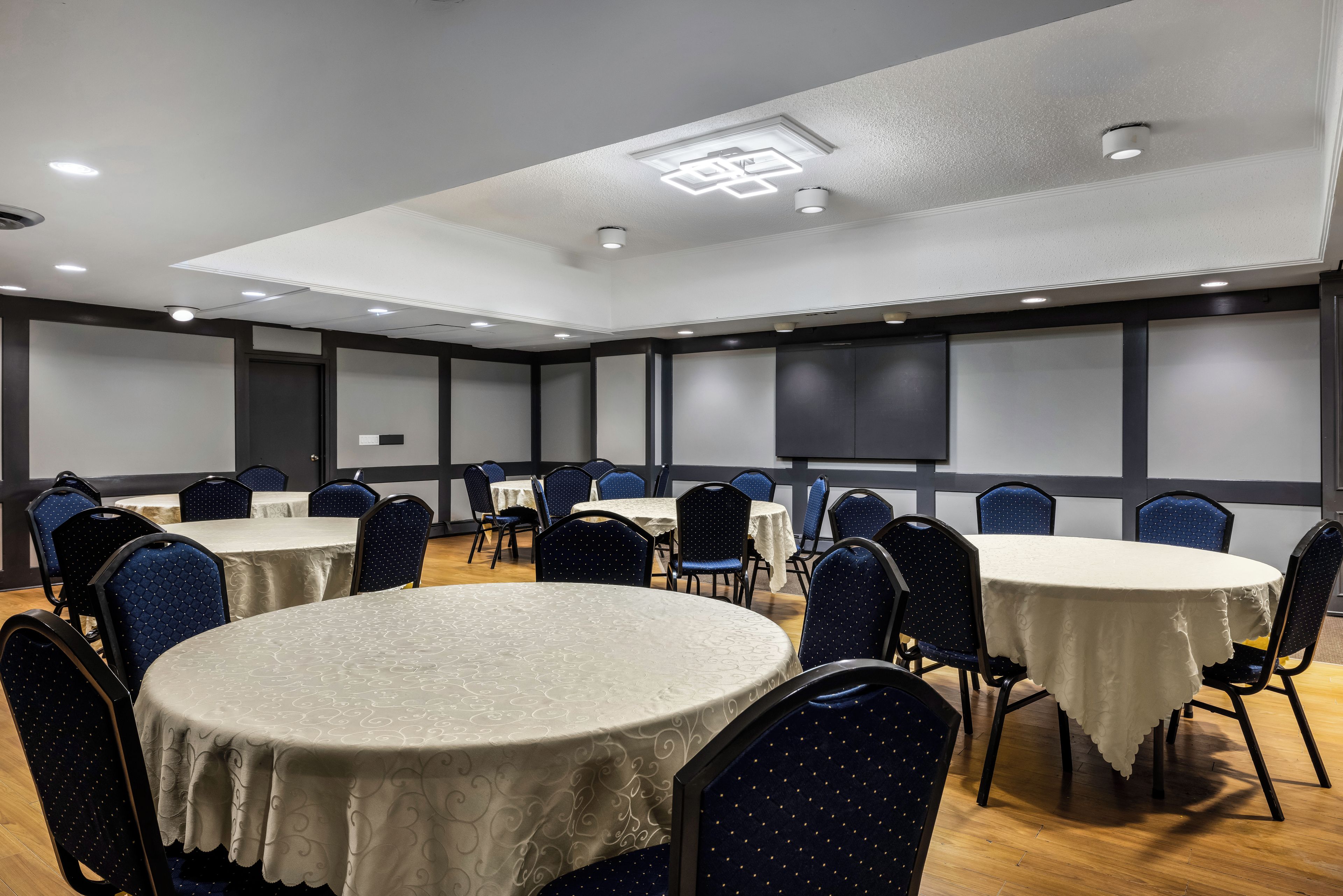 A conference room with round tables, chairs, and a projector screen on the wall.